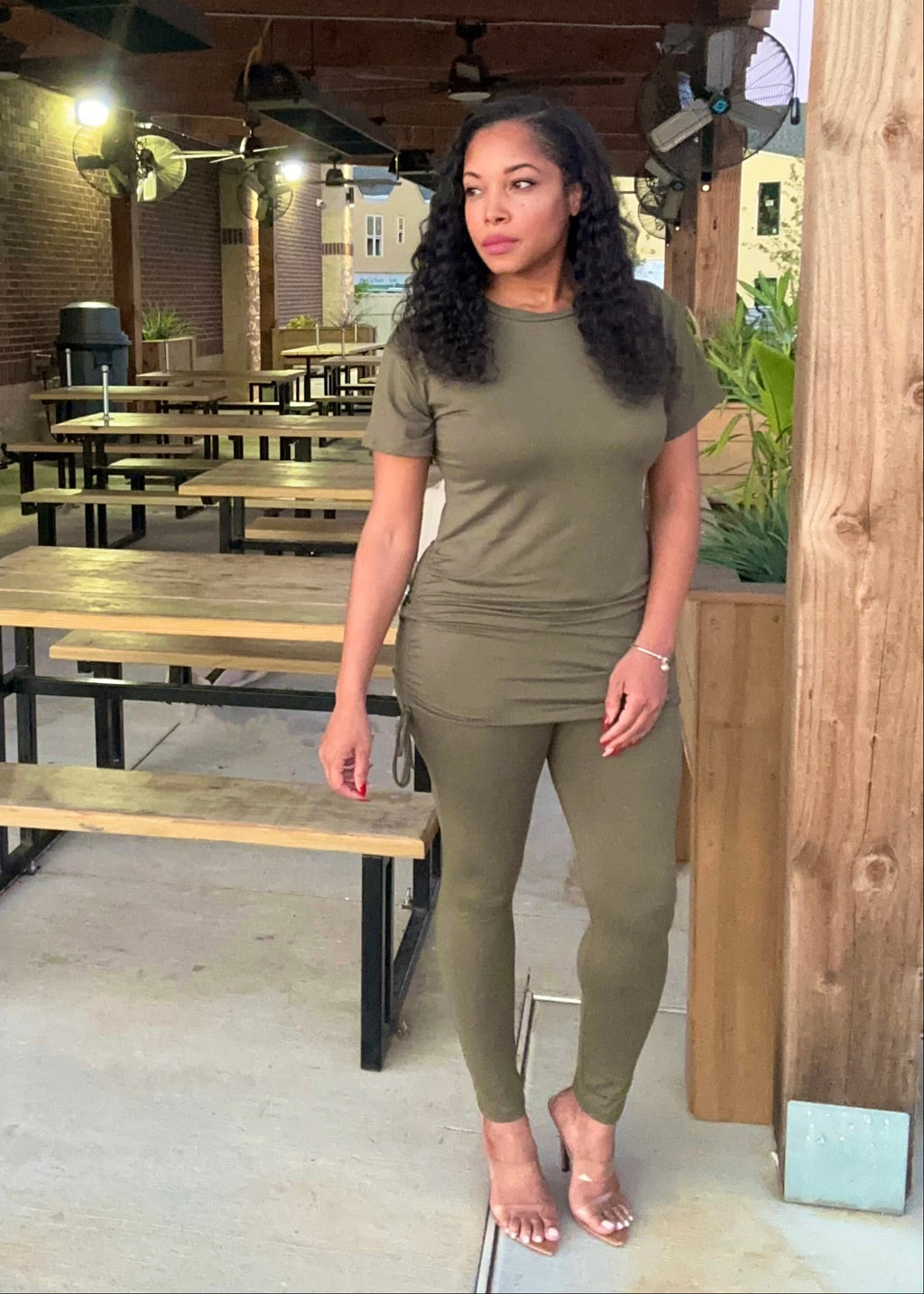 Woman in olive green outfit standing in an outdoor seating area with tables and benches.