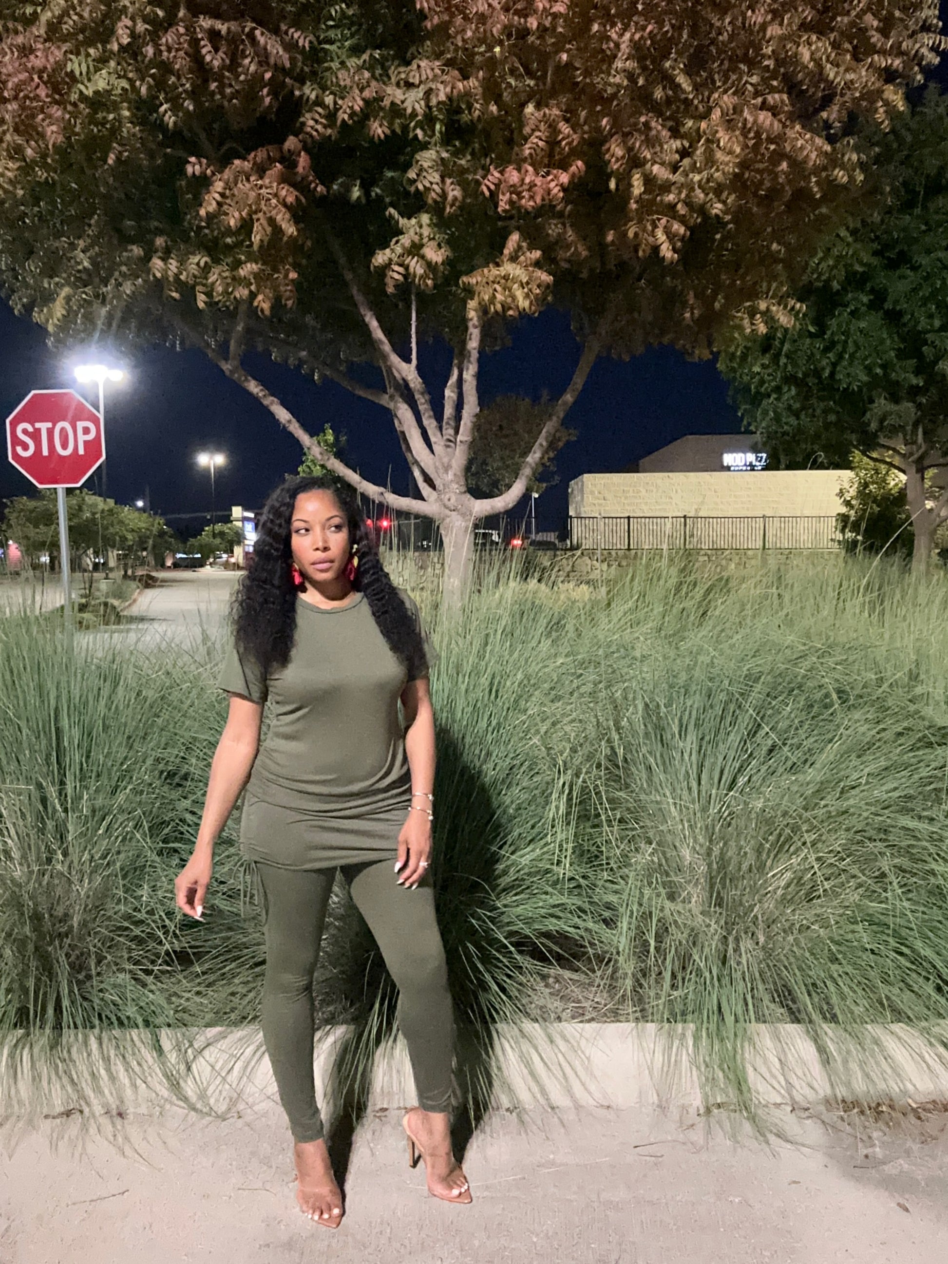Woman in a green outfit standing outdoors at night with trees and a stop sign in the background.