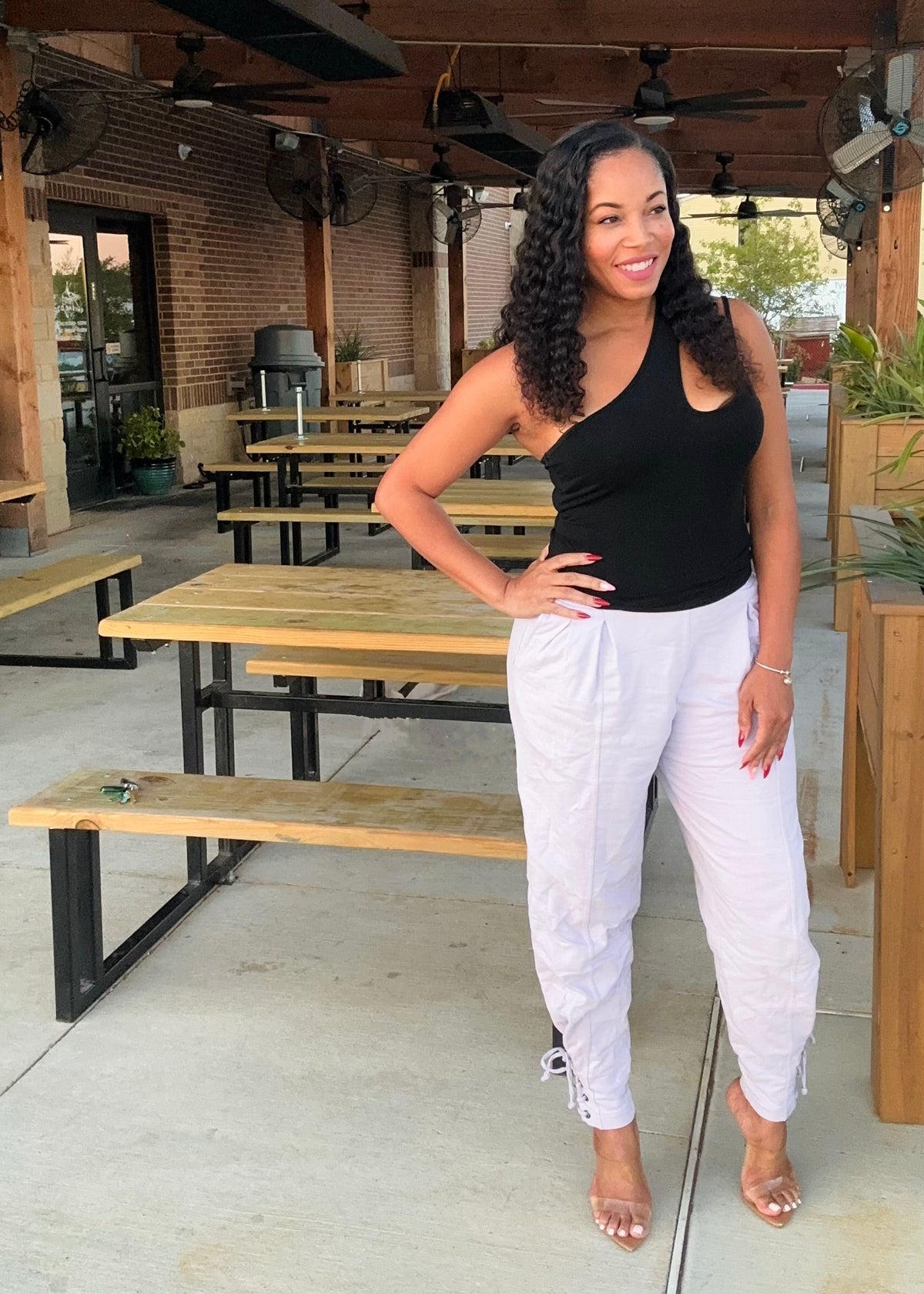 Woman in black top and white pants standing in an outdoor setting with tables and benches.