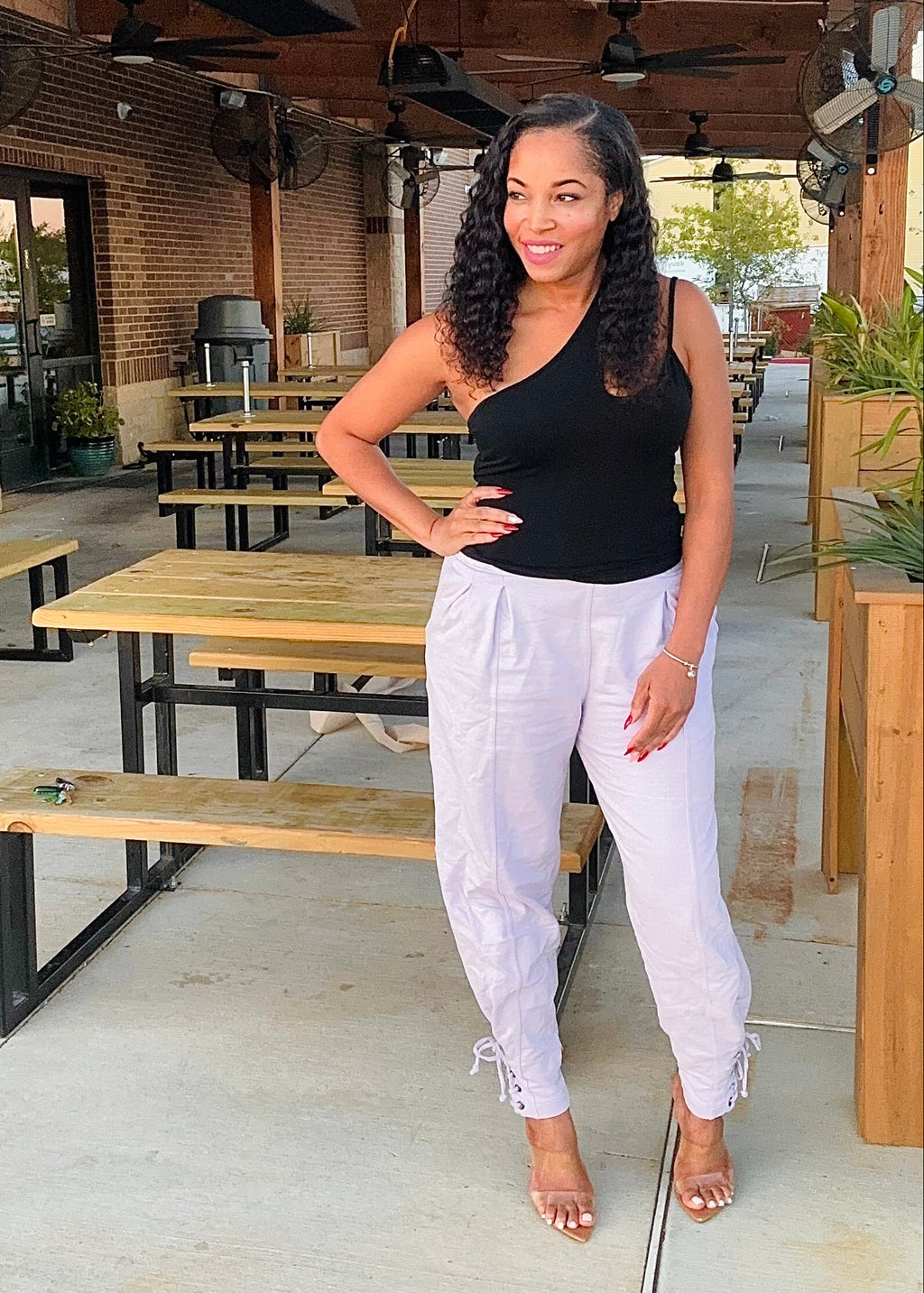 Woman in black top and white pants standing in an outdoor setting with tables and chairs.