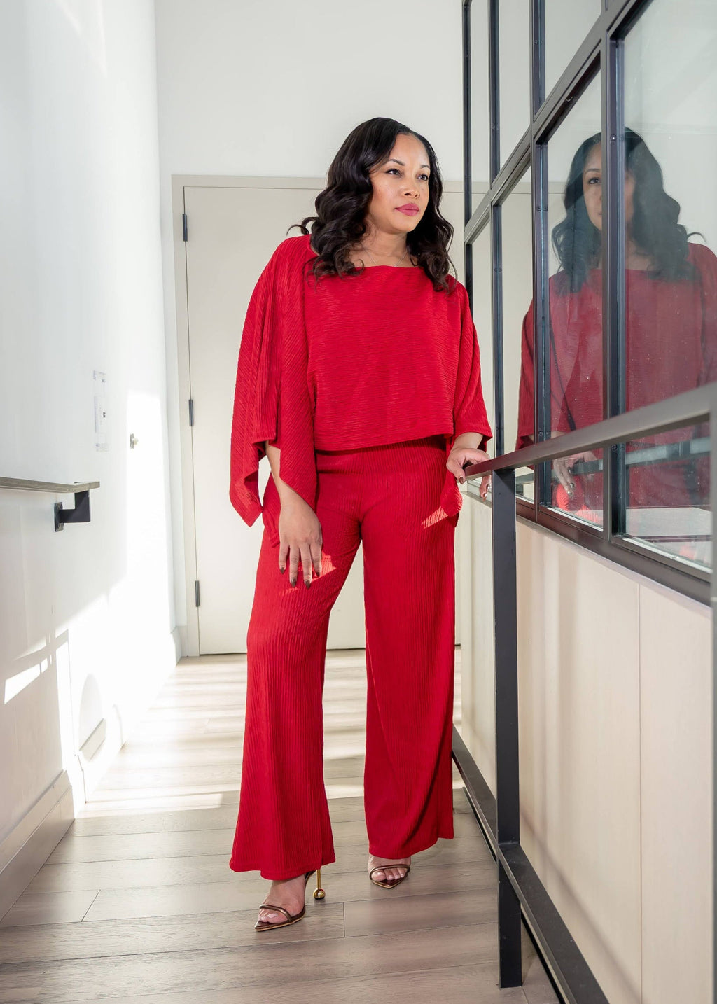 Woman in a red outfit standing in a modern interior setting with glass walls.